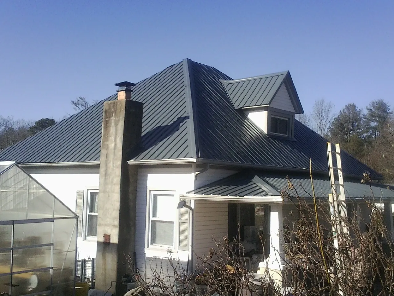 Dark blue standing seam metal roof on a white farmhouse with dormer — Slate & Tile Roof Repair by Roofing Brothers in Wild Rose