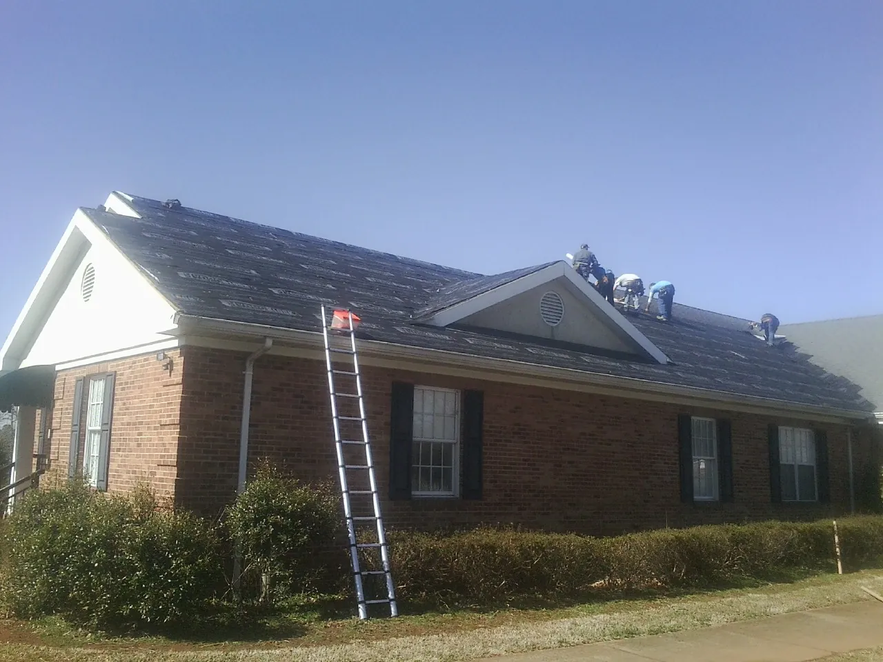 Crew tearing shingles off a brick ranch roof with a ladder set — Metal Roof Repair work by our crew in Wild Rose