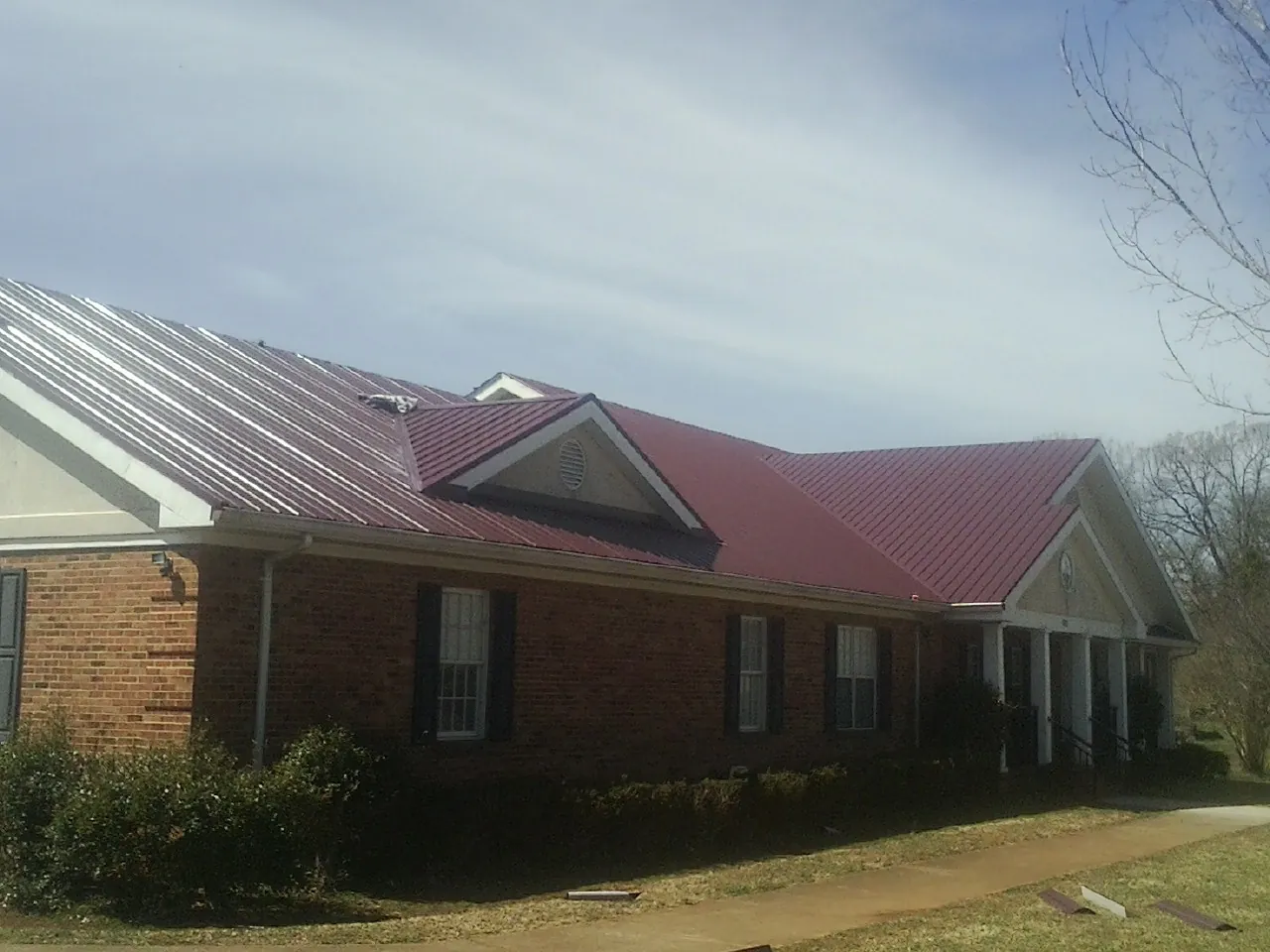 Red metal roof with gabled entries on a long brick building, from a Hail Damage Roof Repair job in Wild Rose