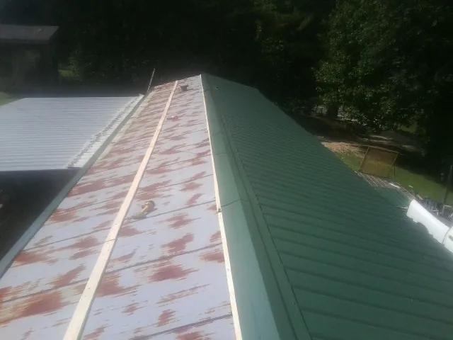 Old rusted panels beside newly installed green metal roofing — Wind Damage Roof Repair by Roofing Brothers in Wild Rose