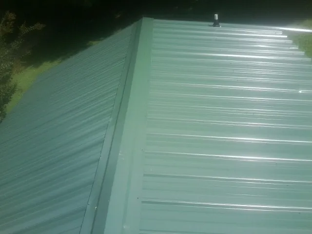New green metal panels meeting at the ridge of a roof — Flat Roof Repair work by our crew in Wild Rose