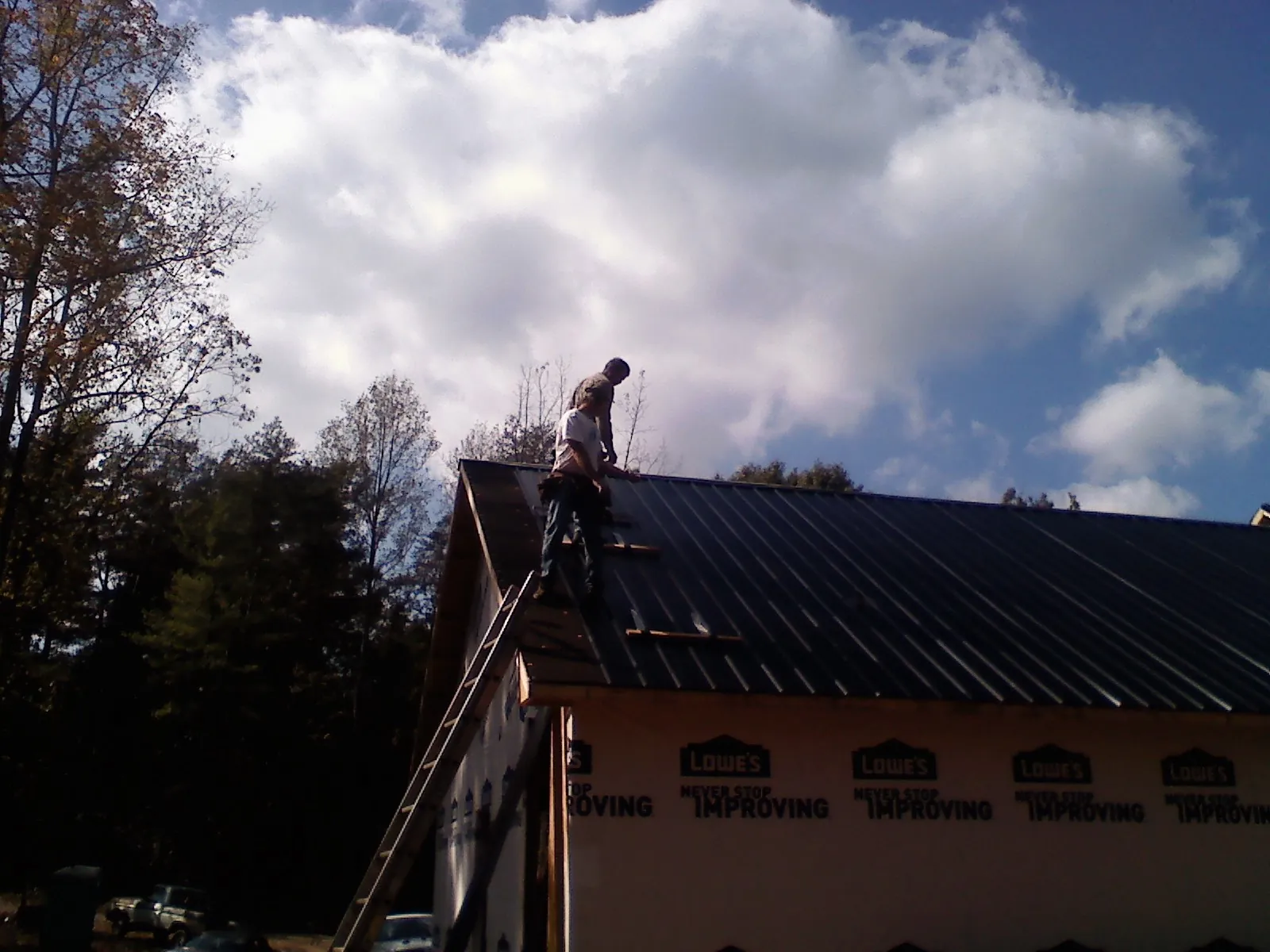 Roofer fastening dark metal panels high against a cloudy sky, from a Roof Inspection job in Wild Rose