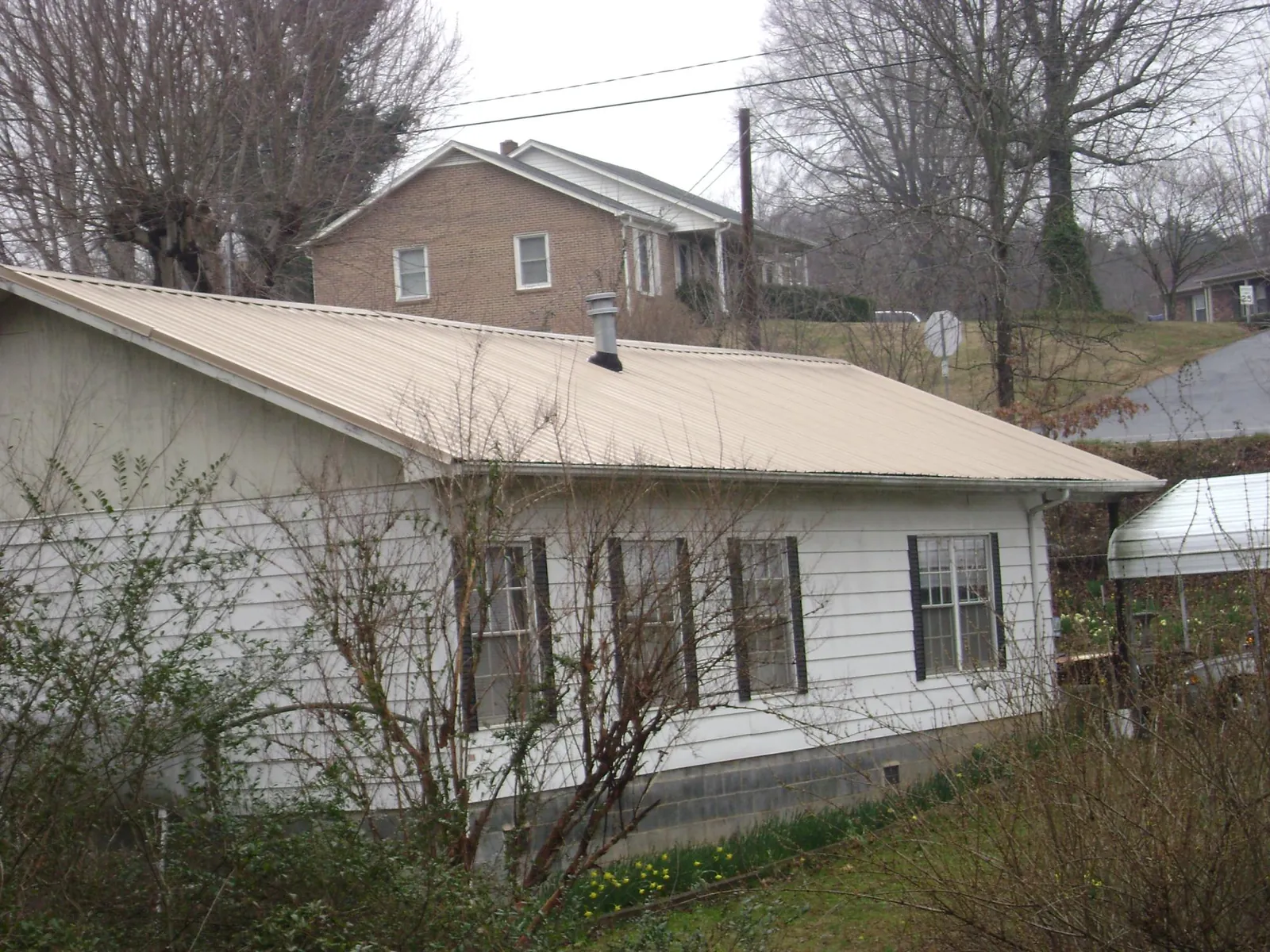 Tan metal roof on a white sided house set into a hillside — Commercial Roofing by Roofing Brothers in Wild Rose