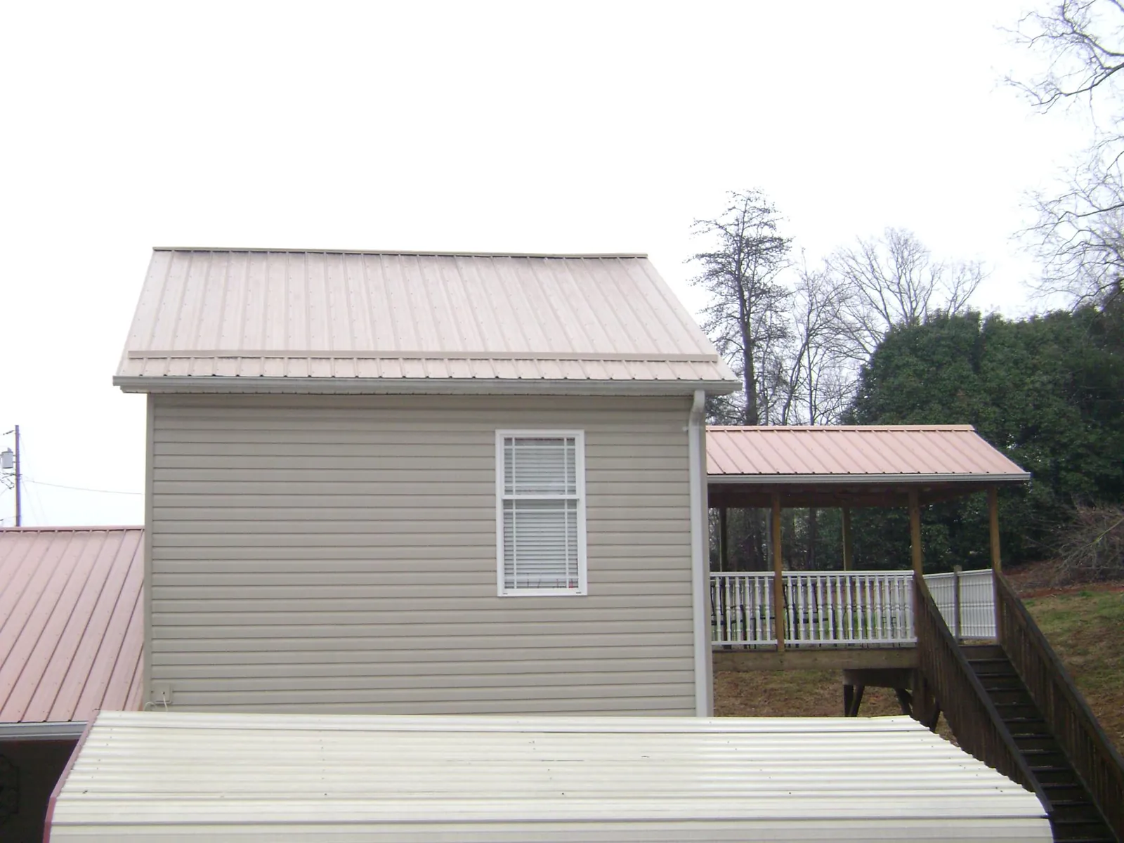 Tan metal roofs on a two story addition and attached porch, from a Roof Replacement job in Wild Rose